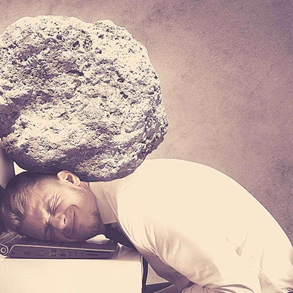 Mann mit Felsbrocken auf dem Kopf, Kopf liegt auf dem Notebook