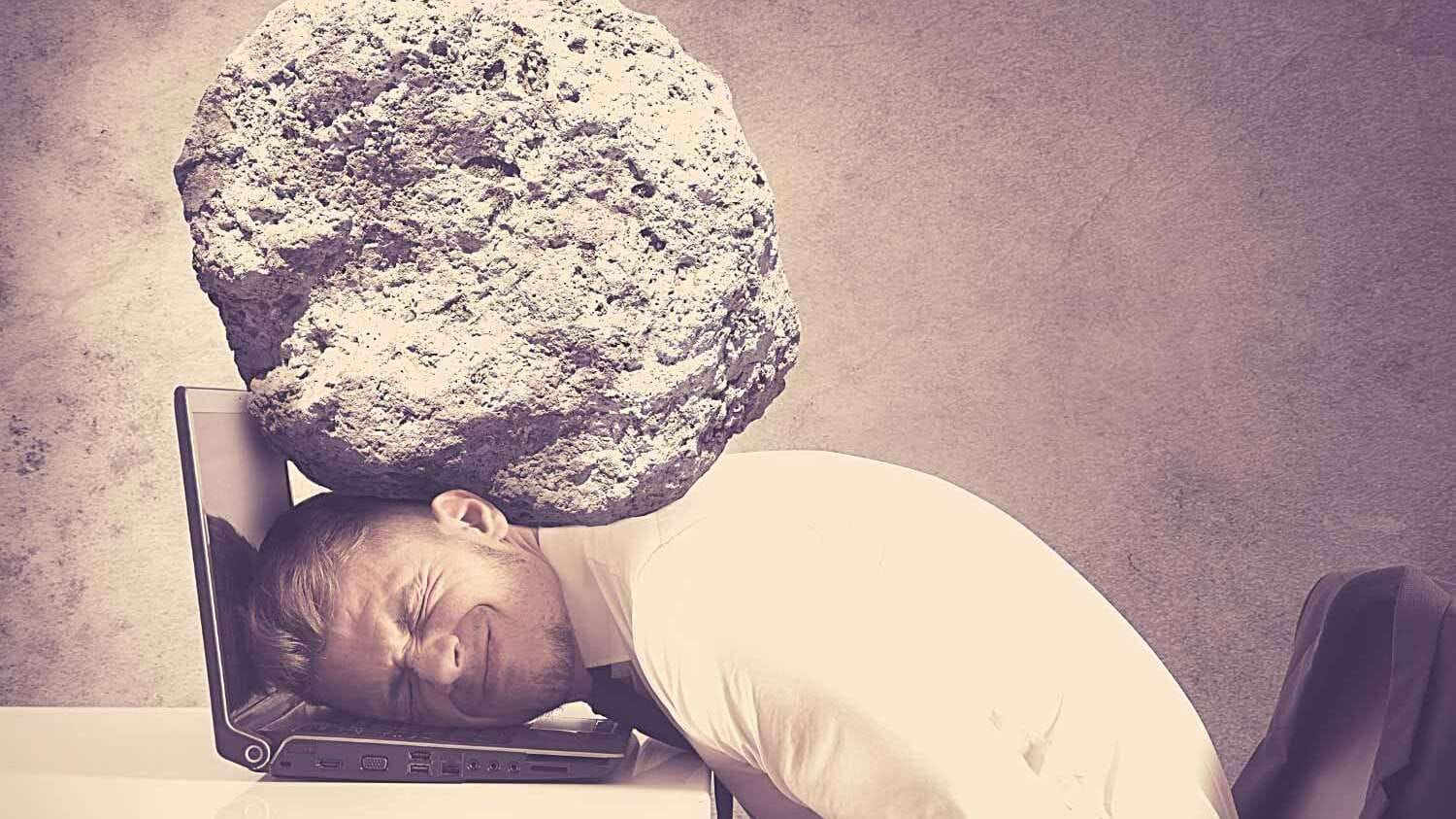 Mann mit Felsbrocken auf dem Kopf, Kopf liegt auf dem Notebook