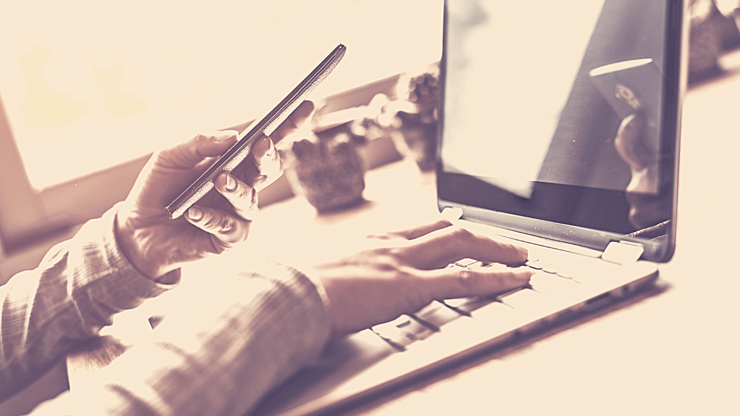 Rechte Hand an der Tastatur beim digitalem Arbeitendes Notebooks mit Smartphone in der anderen Hand